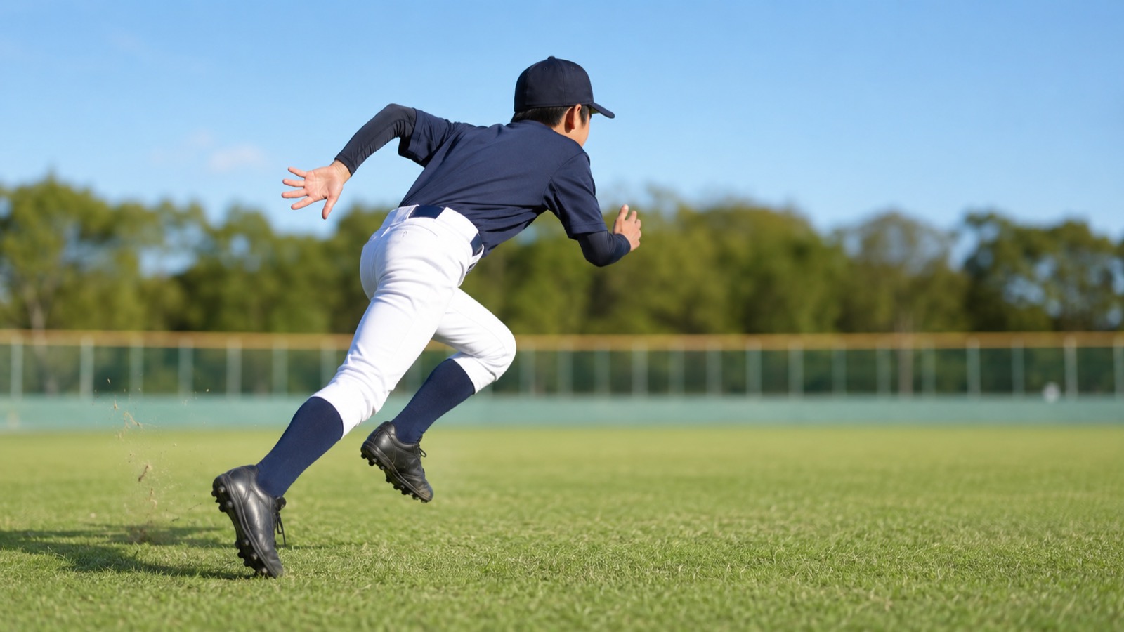 青空の下、外野の芝生でダッシュのスタートを切る少年野球のピッチャー。短い距離を全力で走り出す一歩目