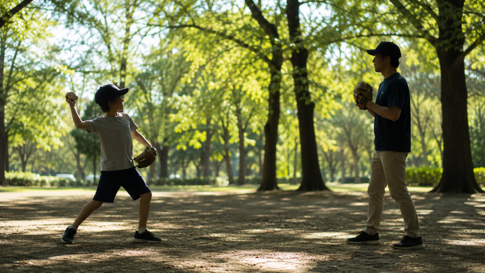公園で親子がキャッチボールをする場面。近い距離で向かい合い、子どもが相手の胸をねらってボールを投げている。晴れた日の午後のやわらかい光