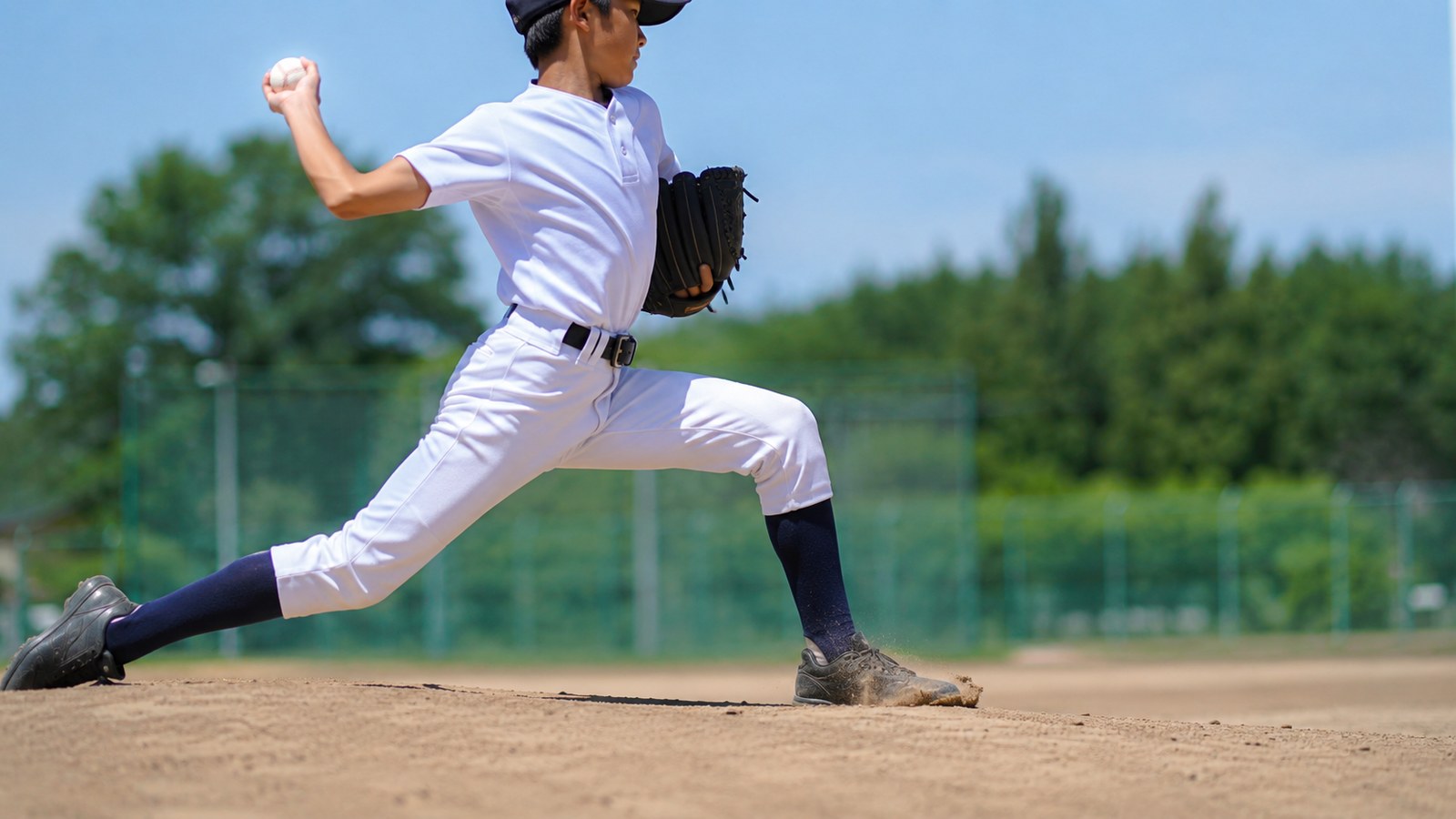 晴れた日中のグラウンドで、踏み出した足を着地させた瞬間の少年野球のピッチャー。踏み出し足のつま先がホーム方向を向いている、ローアングルの横からのアングル